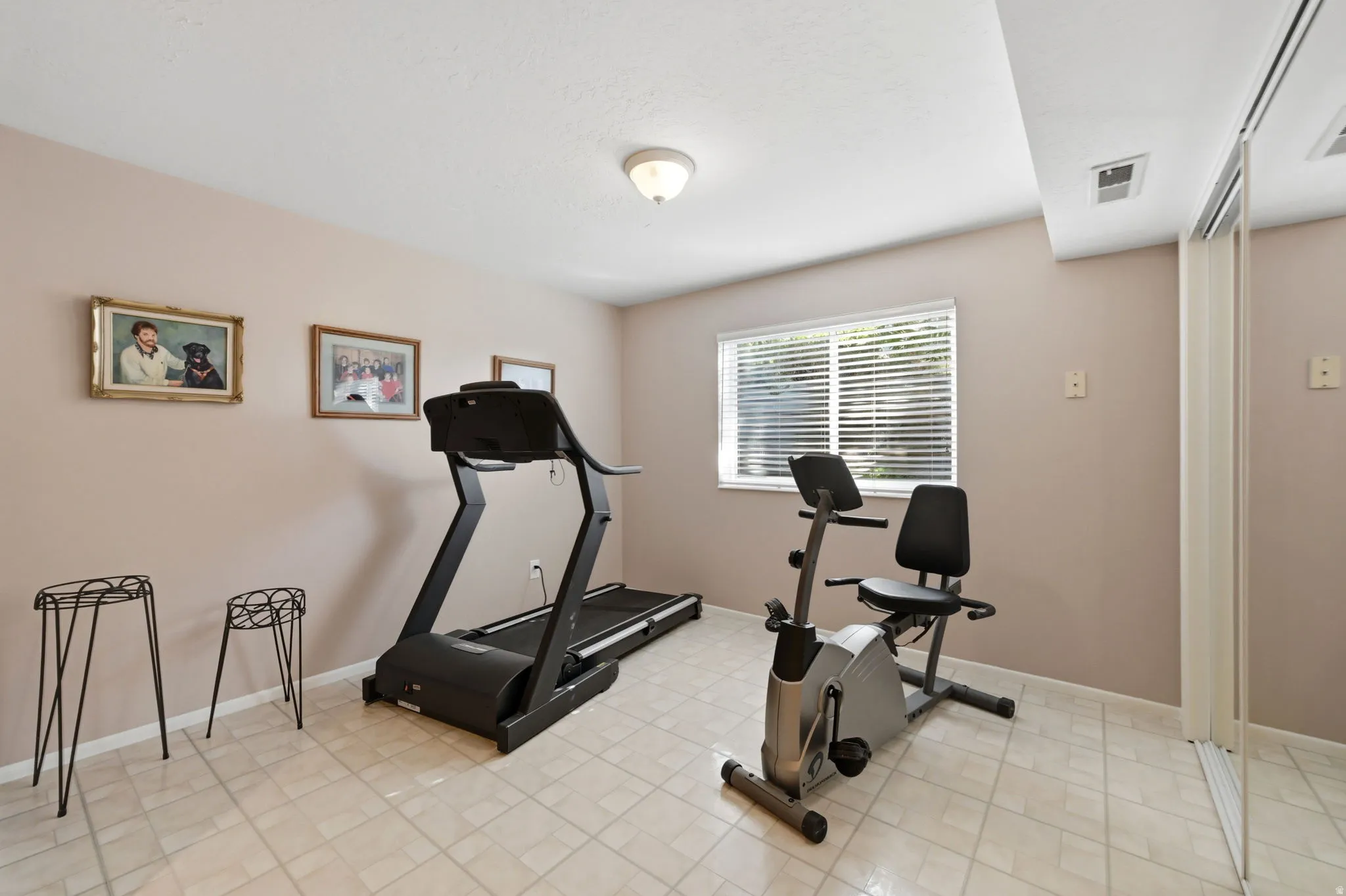 Bedroom or office/exercise room, neutral-toned walls, tiled flooring, window with horizontal blinds, ceiling-mounted light fixture, and mirrored closet doors