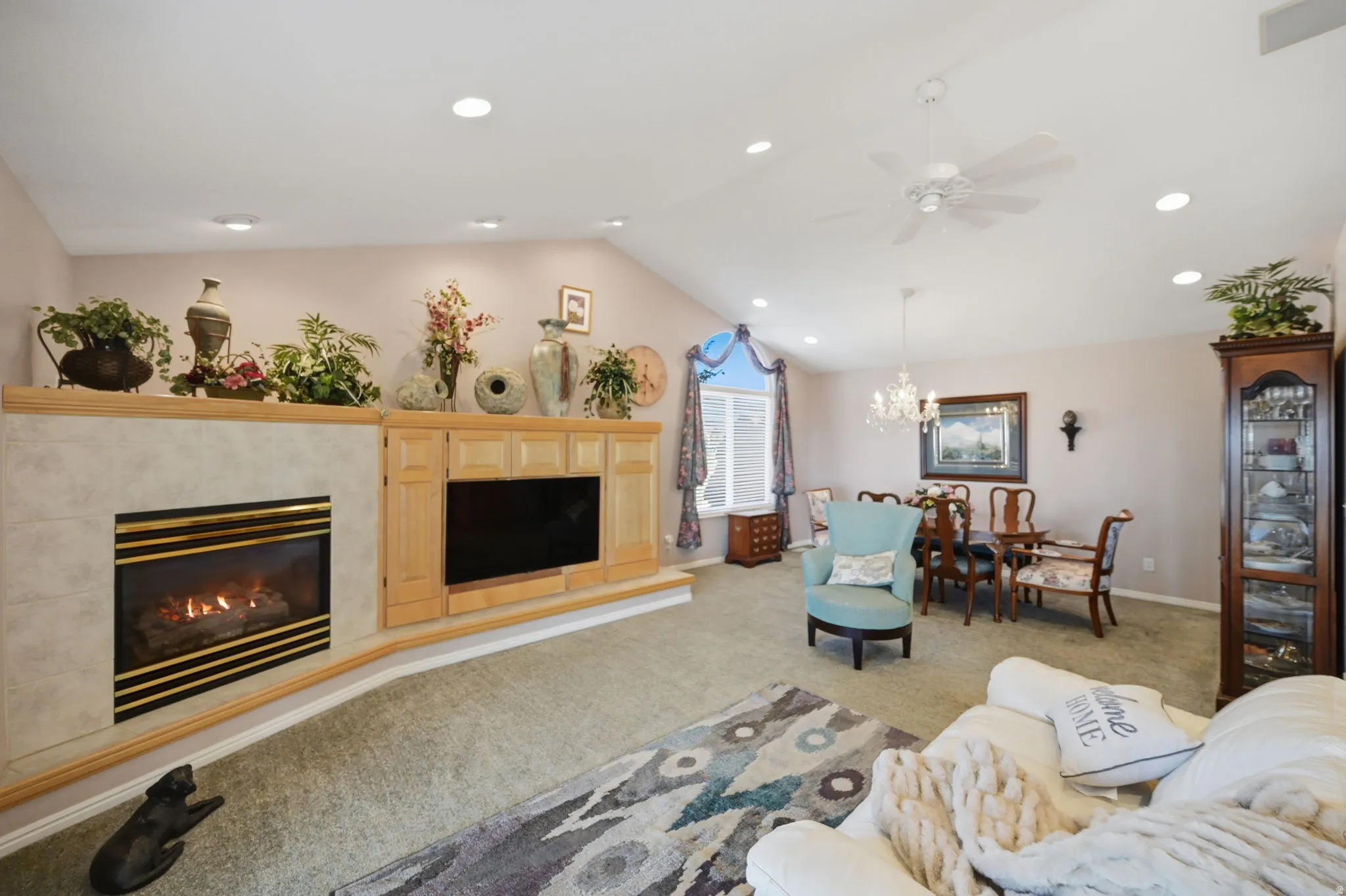 Vaulted ceiling with recessed lighting, built-in fireplace with tile surround, built-in media cabinetry, and dining area with chandelier