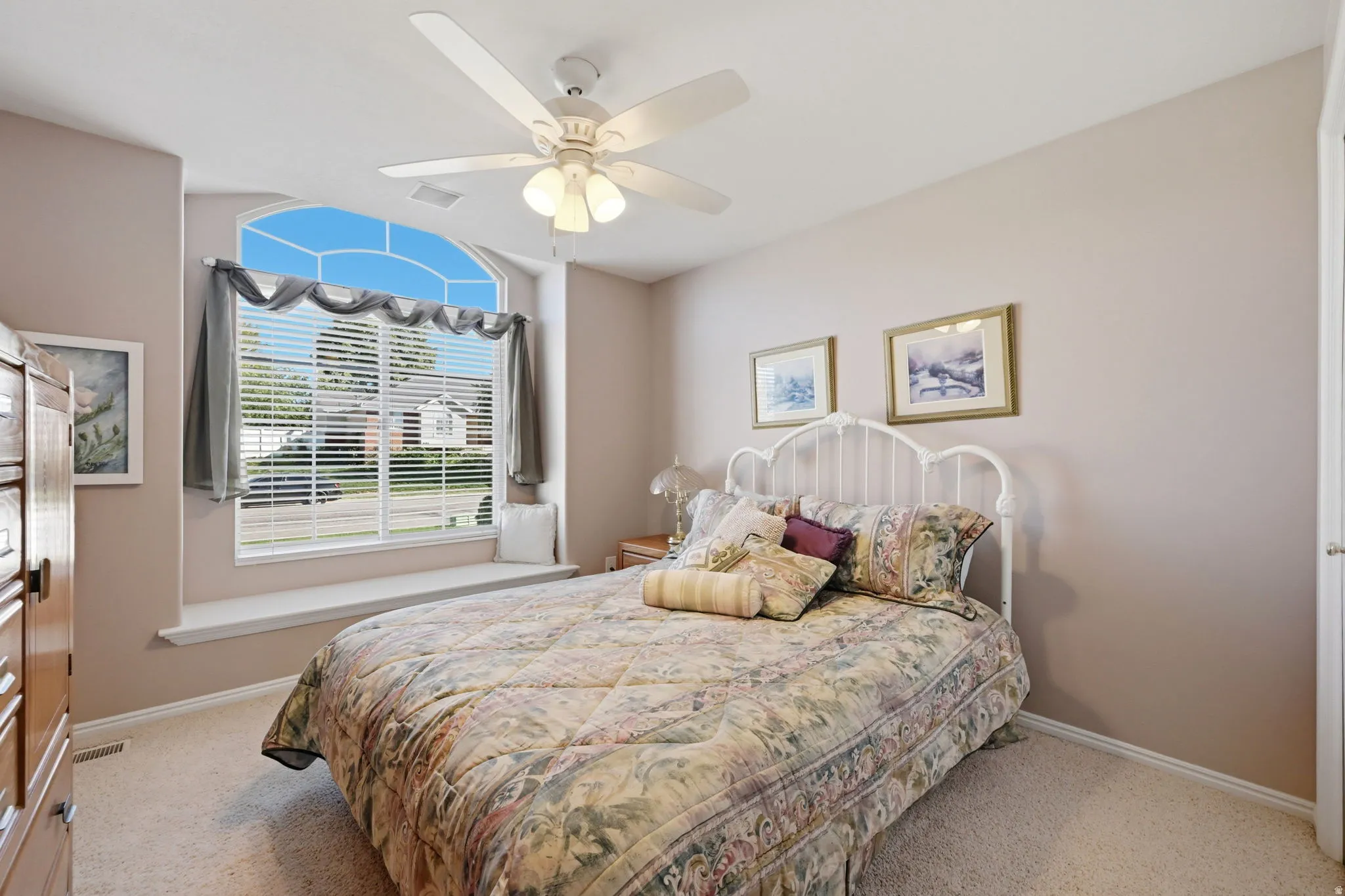 Arched window with integrated window seat, ceiling fan with light fixture, and neutral-toned wall paint