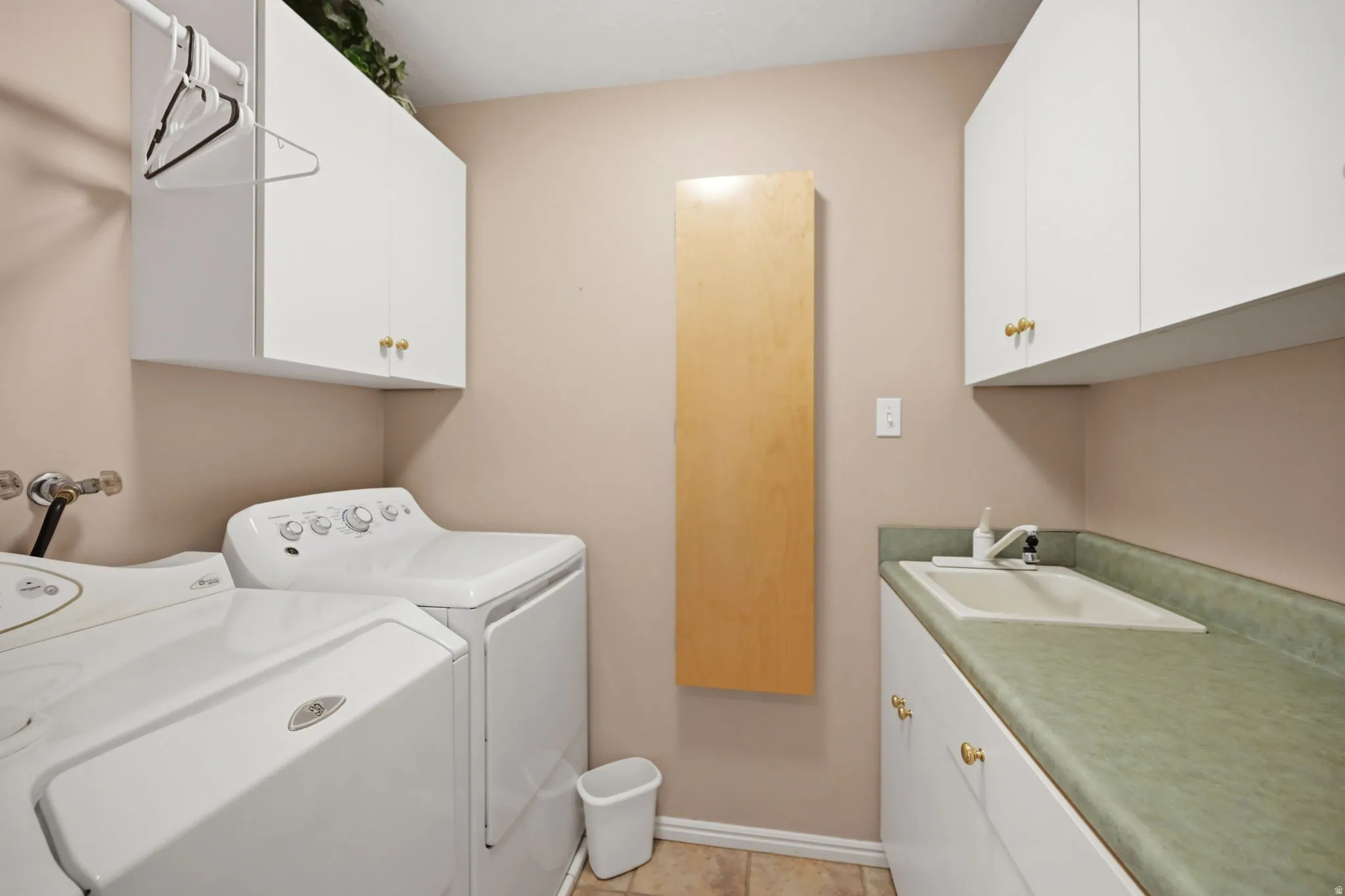 White upper and lower cabinetry with brass-toned hardware, a fixed wall-mounted wooden folding surface, and a utility sink with a light green countertop