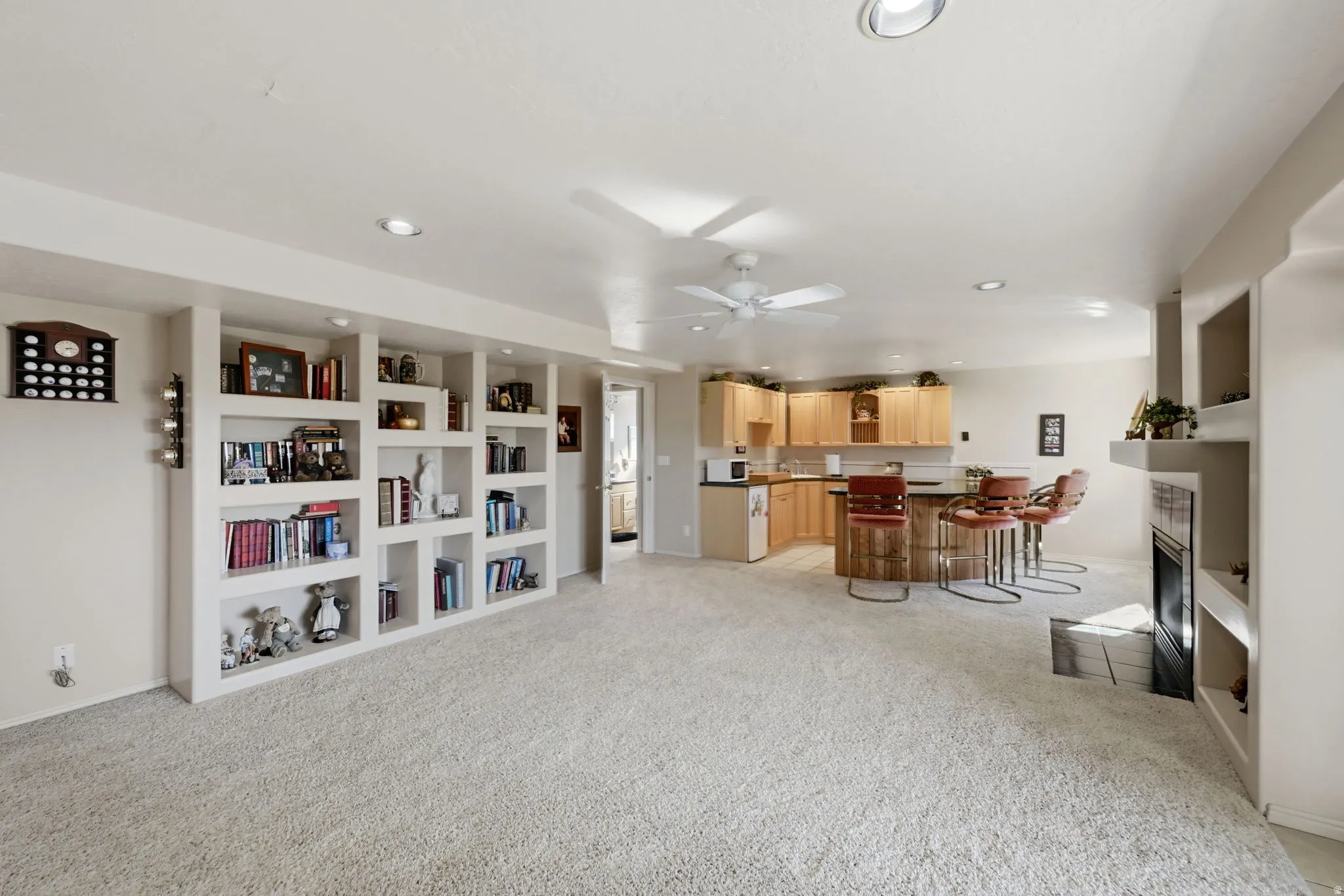 Recessed lighting, ceiling fan, built-in shelving, stone fireplace with hearth, and a bar area with wood cabinetry and a dark countertop