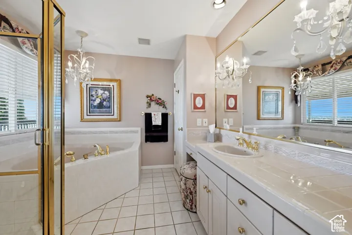 primary bathroom with tile countertop, integrated sink, large corner tub, walk-in shower, and gold-tone faucet