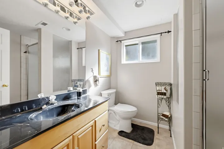Hardwood vanity with a black countertop and integrated sink, a large mirror, and a shower with a sliding glass door