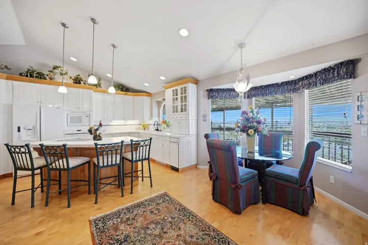 Kitchen and dining area featuring light wood-finish flooring, white cabinetry, a kitchen island with seating, a vaulted ceiling, and multiple windows