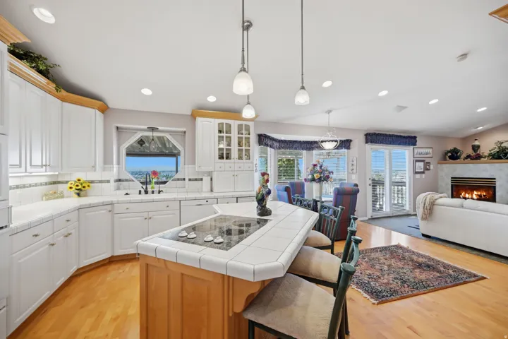 Open-concept kitchen featuring white cabinetry, tile countertops, and a central island with cooktop and built in oven