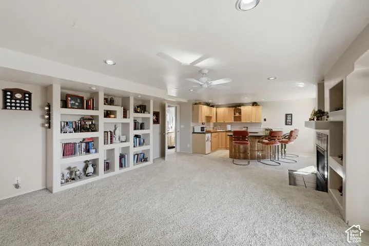 Recessed lighting, ceiling fan, built-in shelving, stone fireplace with hearth, and a bar area with wood cabinetry and a dark countertop