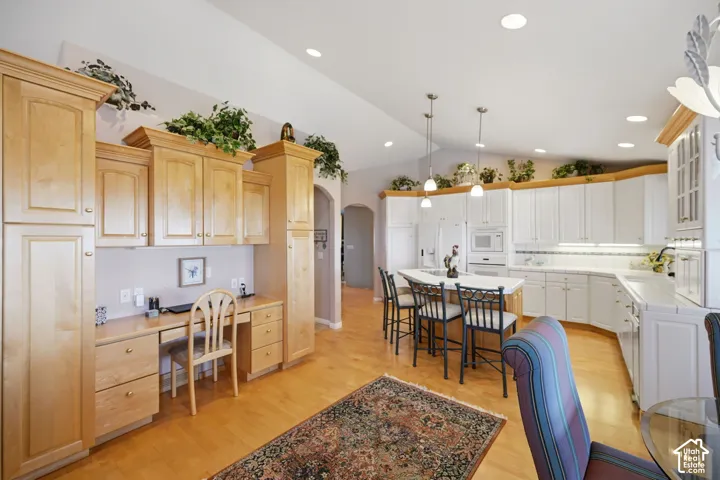 Expansive kitchen with a vaulted ceiling, recessed lighting, white cabinetry, a central island with pendant lighting, cabinetry with desk and light wood-finish flooring