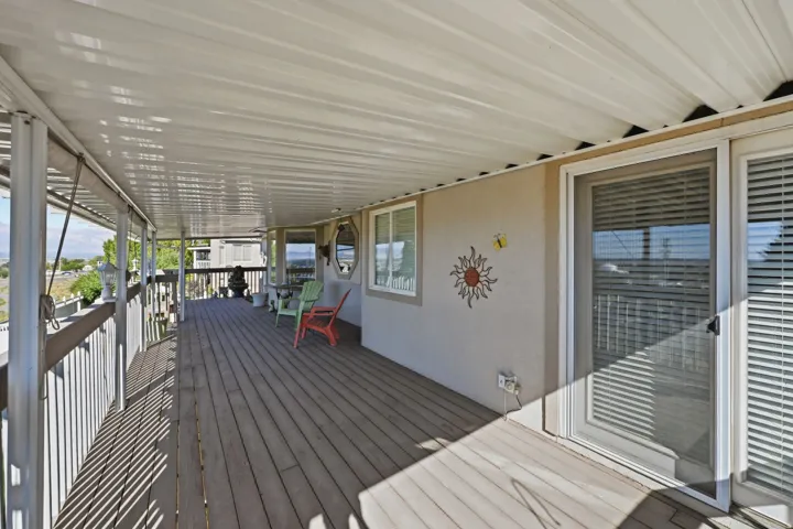 Expansive covered deck with wood-finish flooring, white railing, multiple windows, and sliding doors