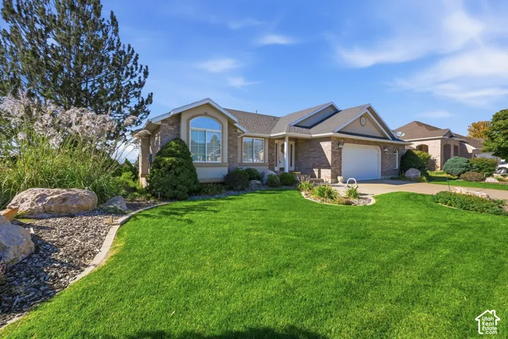 Brick exterior with a gabled roofline, arched window, attached garage, and manicured landscaping with decorative rocks