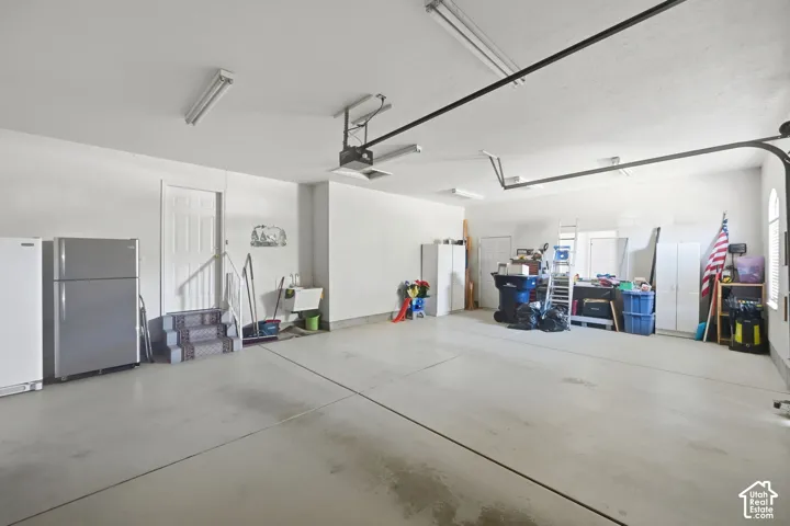 Spacious garage with high ceilings, garage sized extra space for storage, multiple fluorescent light fixtures, and a utility sink