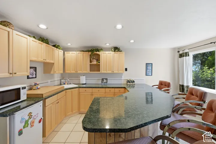 Kitchenette with recessed lighting, wood cabinetry, green speckled countertops, built-in sink, and tile flooring