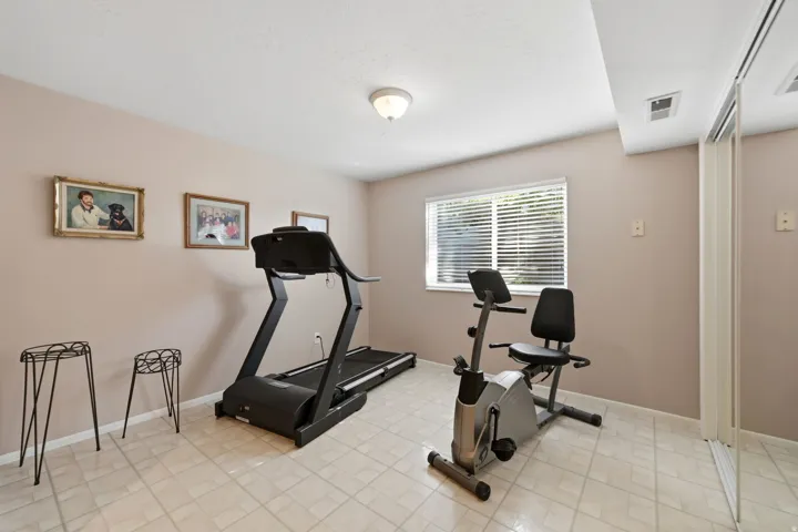Bedroom or office/exercise room, neutral-toned walls, tiled flooring, window with horizontal blinds, ceiling-mounted light fixture, and mirrored closet doors