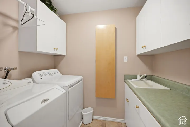 White upper and lower cabinetry with brass-toned hardware, a fixed wall-mounted wooden folding surface, and a utility sink with a light green countertop