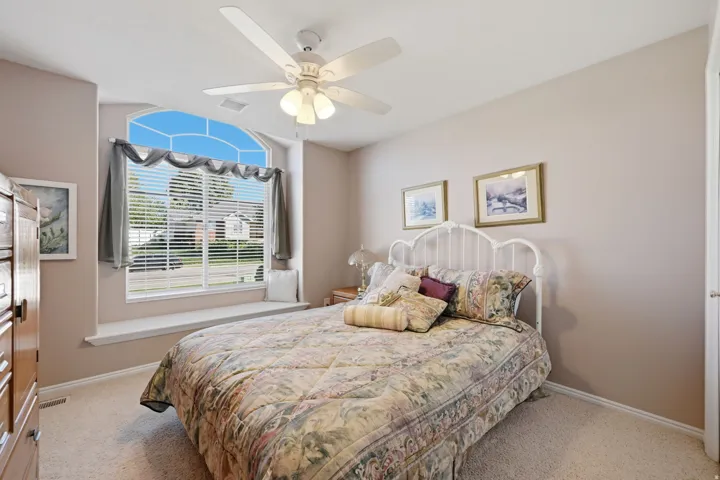 Arched window with integrated window seat, ceiling fan with light fixture, and neutral-toned wall paint