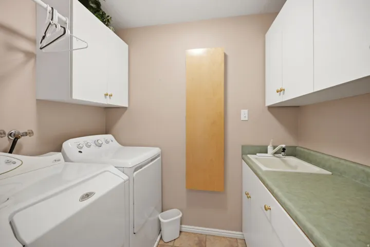 White upper and lower cabinetry with brass-toned hardware, a fixed wall-mounted wooden folding surface, and a utility sink with a light green countertop
