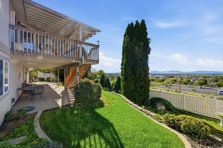 Expansive upper-level deck with wood railing, covered lower-level patio, sloped green lawn, and distant city scenery