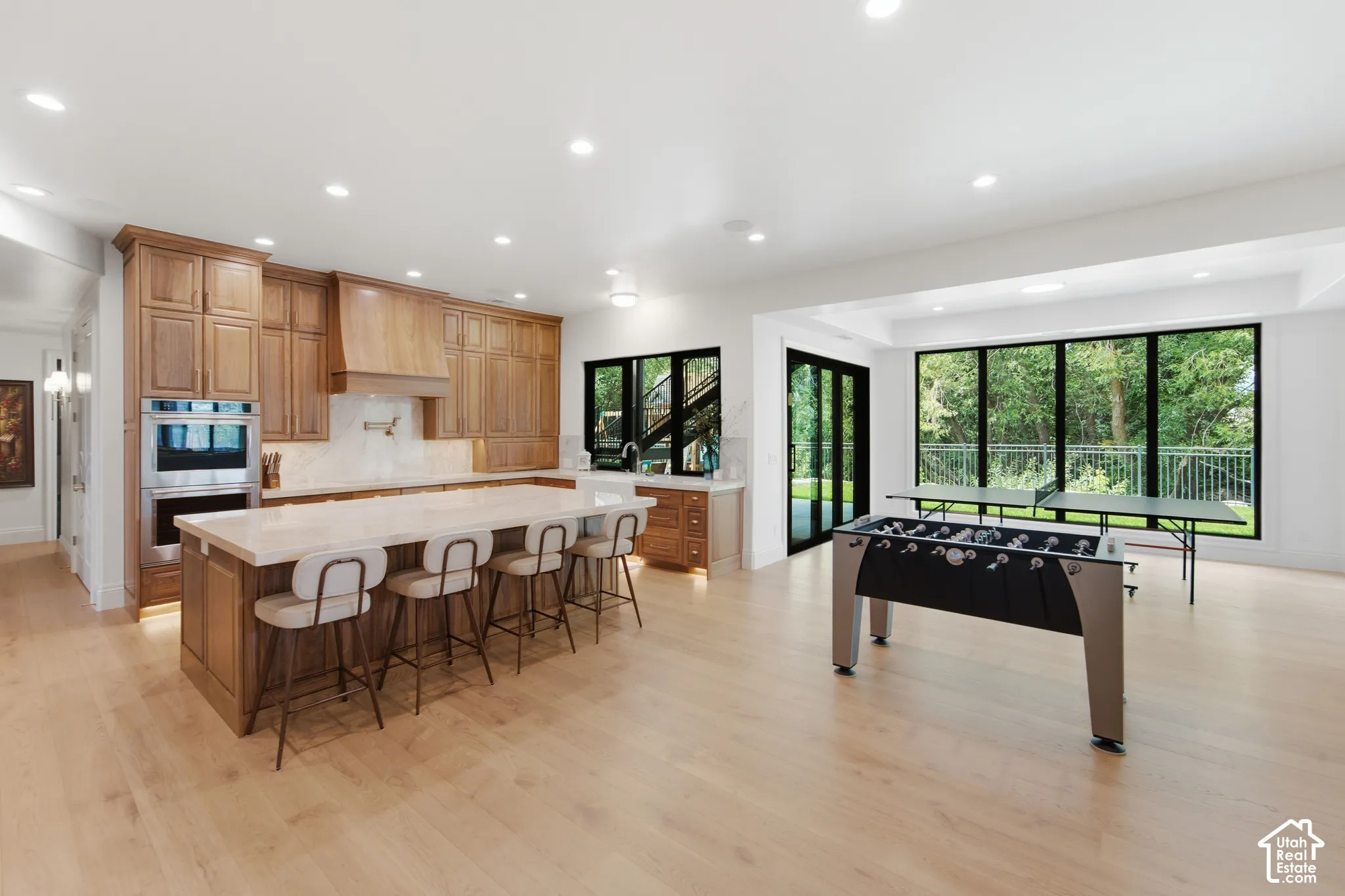 Spacious open-concept living area with wood-finish flooring, a kitchen island with seating, integrated double ovens, and large windows with exterior access