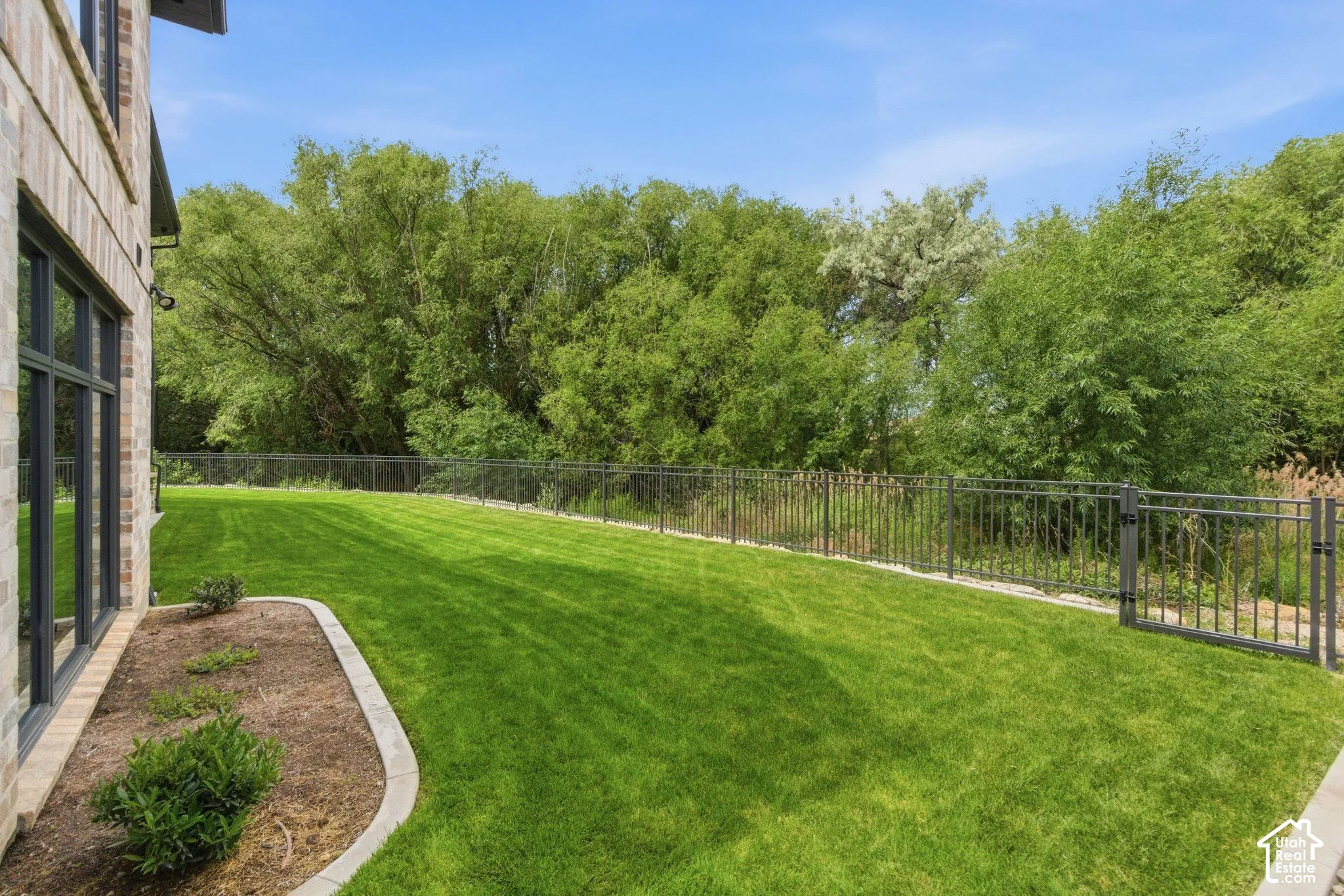 Expansive lawn area with a black metal fence, mature trees, and a landscaped bed with plantings