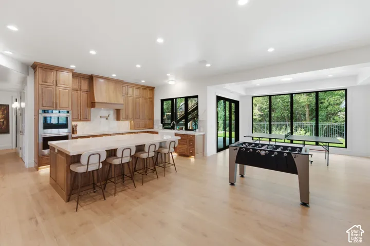 Spacious open-concept living area with wood-finish flooring, a kitchen island with seating, integrated double ovens, and large windows with exterior access