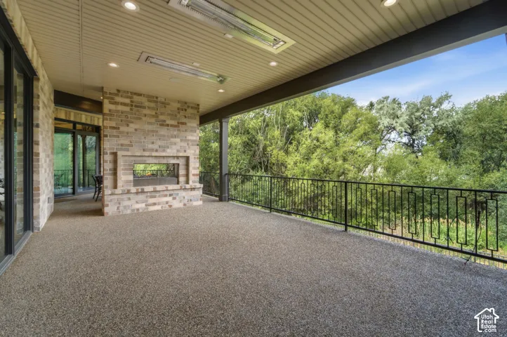 Spacious covered deck with an exposed aggregate surface, a built-in brick fireplace, ornamental metal railing, heaters in ceiling