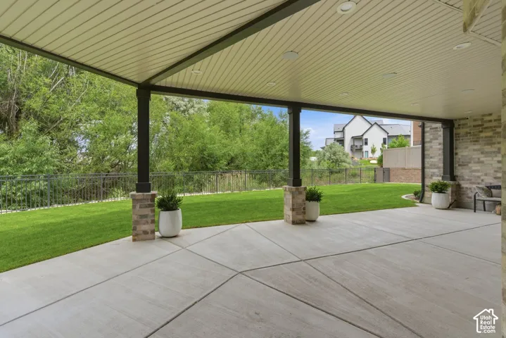 Expansive covered patio with concrete slab flooring, recessed lighting, and brick-clad support columns