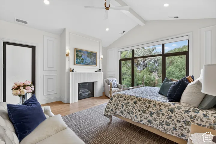 Vaulted ceiling with exposed beams, fireplace with reeded detailing, large window with dark trim, door to deck