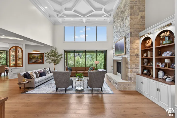19 ft. ceiling with geometric molding, stone-clad fireplace, built-in cabinetry with arched display shelves, wood-finish flooring, and expansive windows