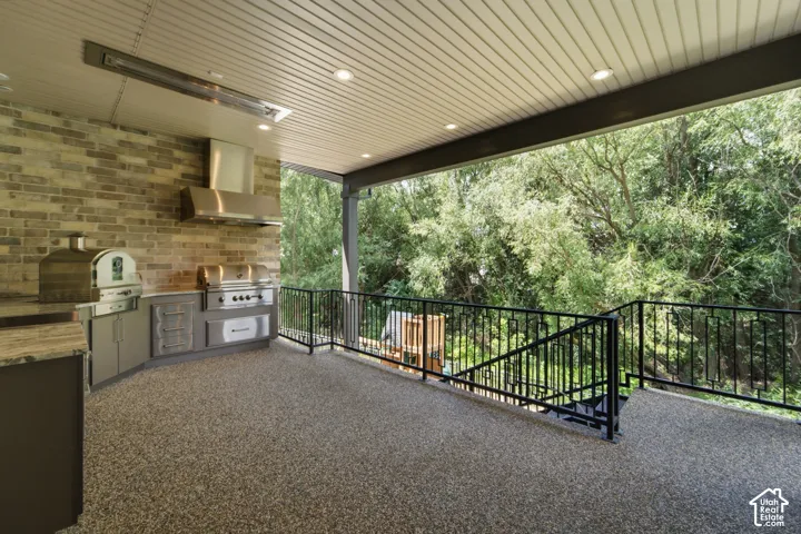 Covered outdoor kitchen featuring a built-in grill, pizza oven, and stainless steel range hood, large burner
