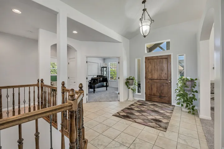 Vaulted entry with an ornate wood door, tile flooring, and a decorative light fixture