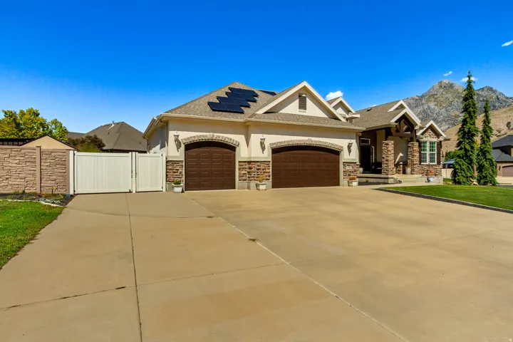 Stucco and stone exterior with a two-car garage, solar panels, and a mountain backdrop