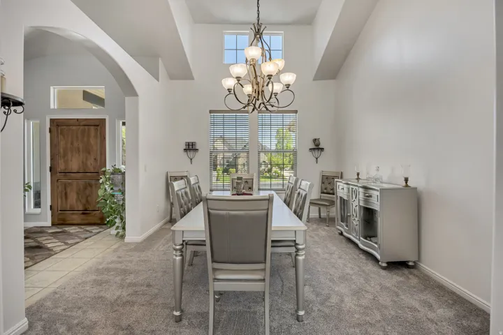 Arched entryway with a wood-finish door and side panel windows, leading to an open dining area with vaulted ceilings and a chandelier