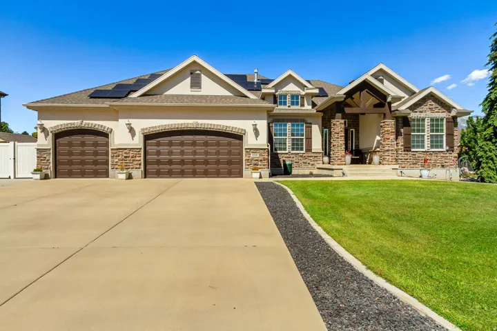 Stucco and stone facade, arched garage doors, concrete driveway, front porch with columns, and solar panels