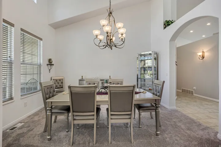Vaulted ceilings with a decorative chandelier, multiple windows with blinds, arched entryways, recessed lighting, and tiled flooring