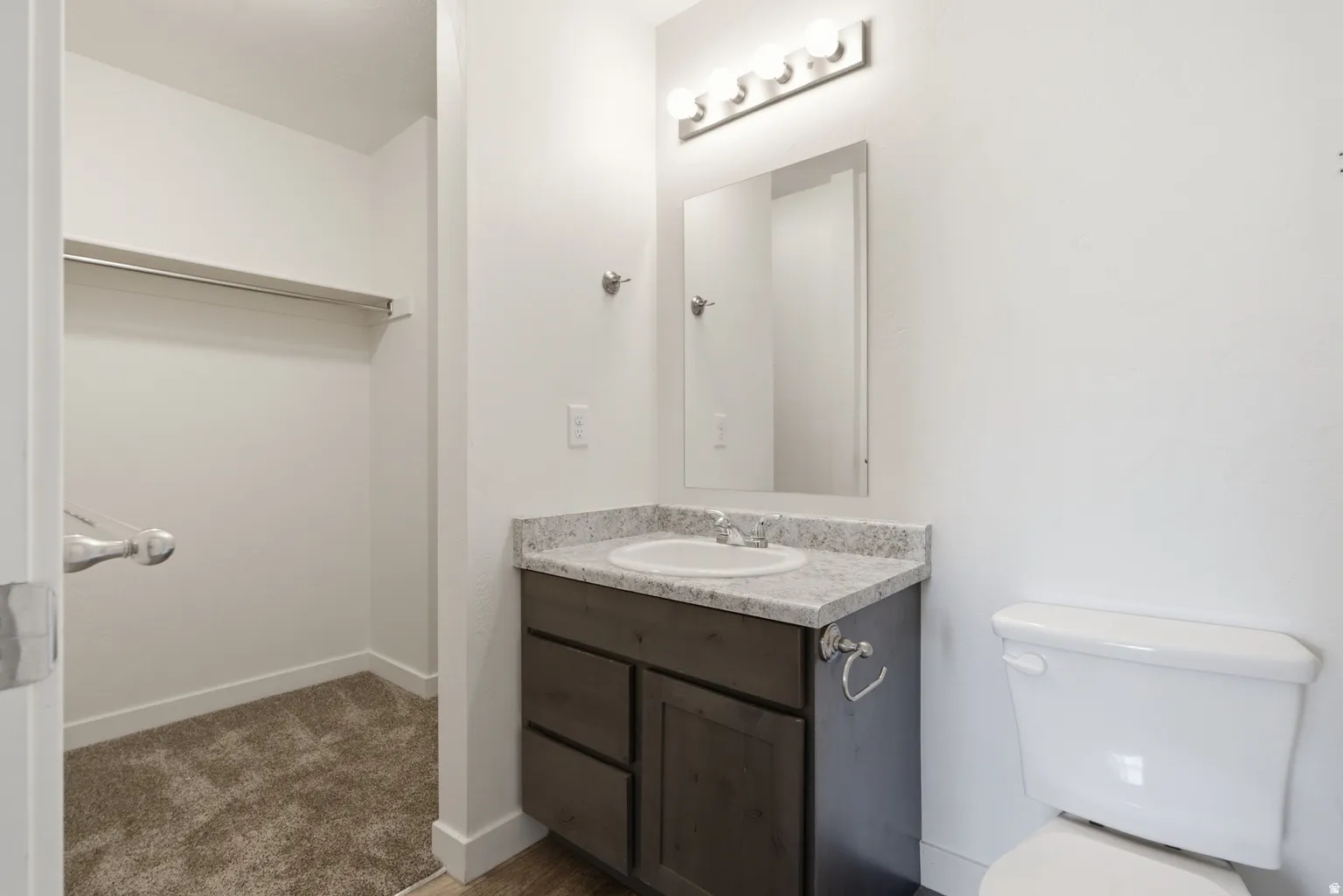 Built-in vanity with a stone-finish countertop and undermount sink, mirrored medicine cabinet, and a walk-in closet with carpet flooring