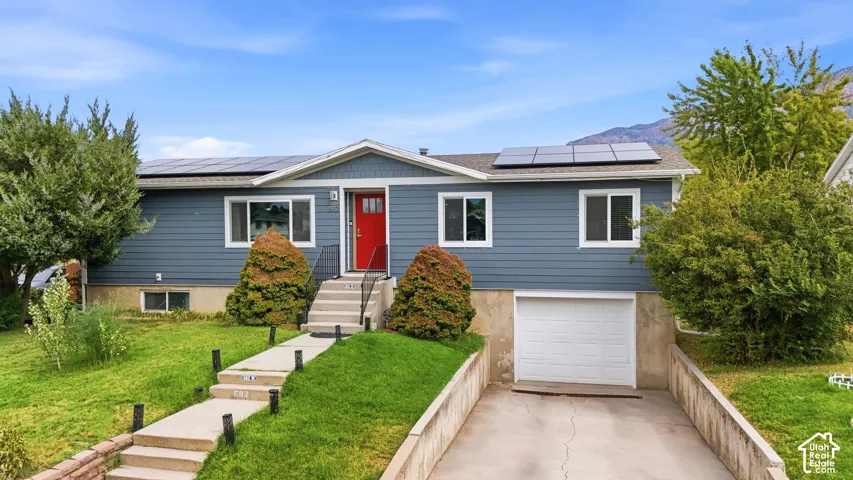 Blue siding exterior with a red entry door, white trim windows, and solar panels
