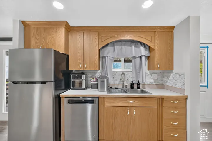 Kitchen featuring wood-finish cabinetry, stainless steel appliances, white countertops, and a tiled backsplash