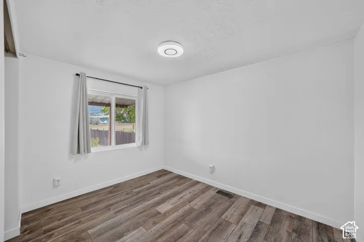 Wood-finish flooring with white baseboards, a window with a white frame, and a flush-mount ceiling light fixture