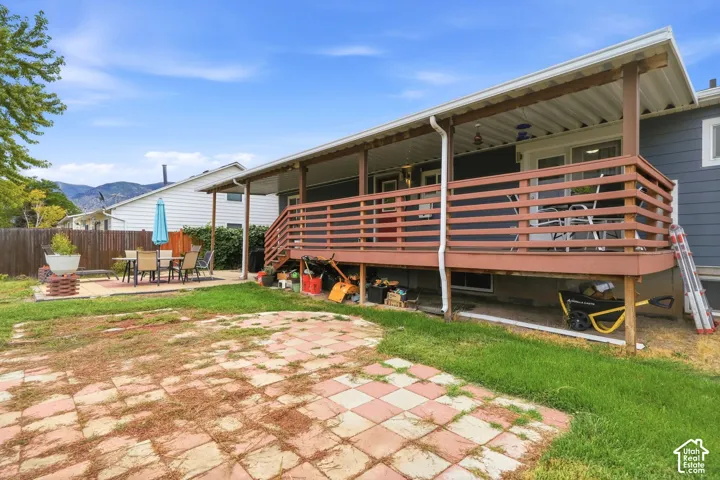 Covered deck with wood railing, leading to a patio with checkered pavers