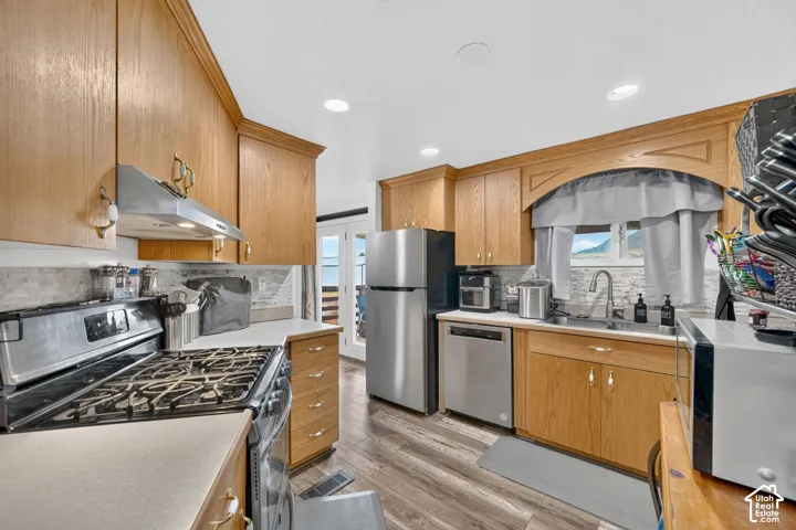 Kitchen featuring wood cabinetry, stainless steel appliances, a tile backsplash, and wood-finish flooring