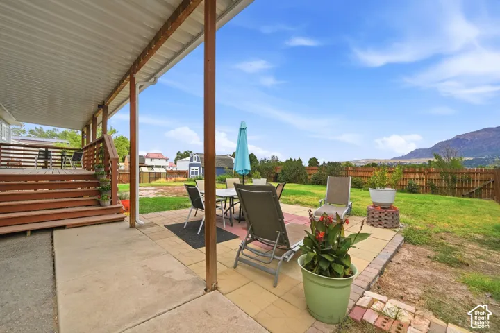 Expansive covered patio with concrete flooring, wood deck with stairs, and a paver stone seating area