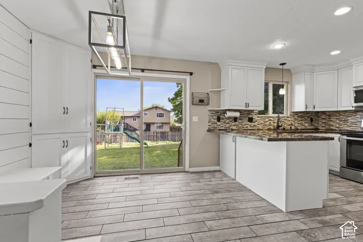 White cabinetry, wood-finish flooring, sliding glass door, mosaic tile backsplash, and stainless steel appliances