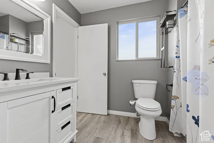 White vanity with black hardware, white countertop, matte black faucet, framed mirror, and wood-finish flooring