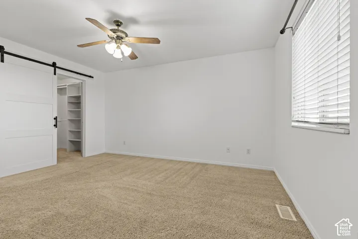 Carpeted room featuring a ceiling fan with light fixture, window with blinds, and barn door entry to a closet with built-in shelving