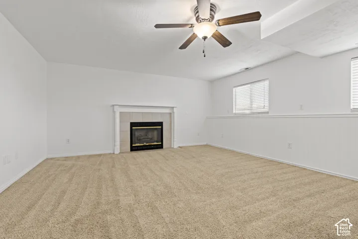 Wall-to-wall carpeting, fireplace with tile surround and mantel, wood-finish ceiling fan, and multiple windows with blinds