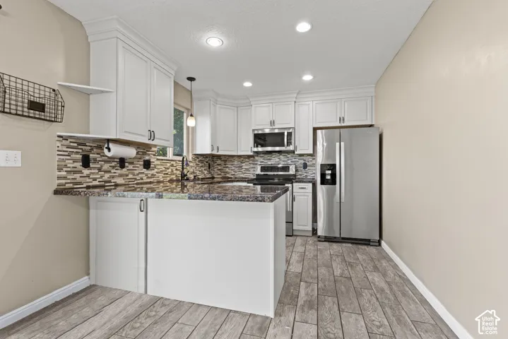 White cabinetry, granite countertops, tile backsplash, wood-finish flooring, and recessed lighting