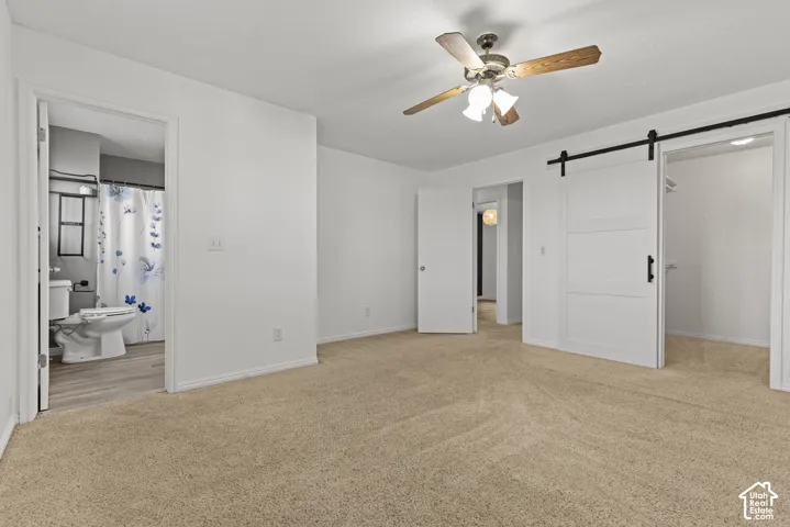 Carpeted flooring, ceiling fan with light fixture, white walls, and a barn door closet entry