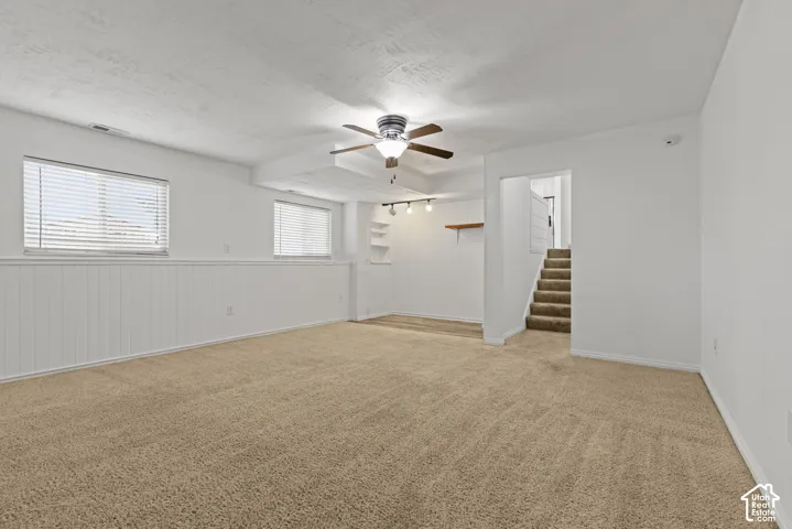 Spacious room featuring carpeting, two windows with blinds, a ceiling fan, and built-in shelving