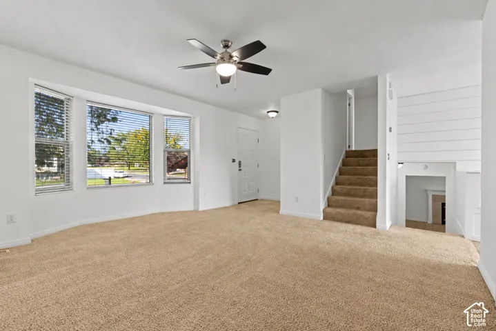 Plush carpeting, a modern ceiling fan, and a bay window featuring horizontal blinds