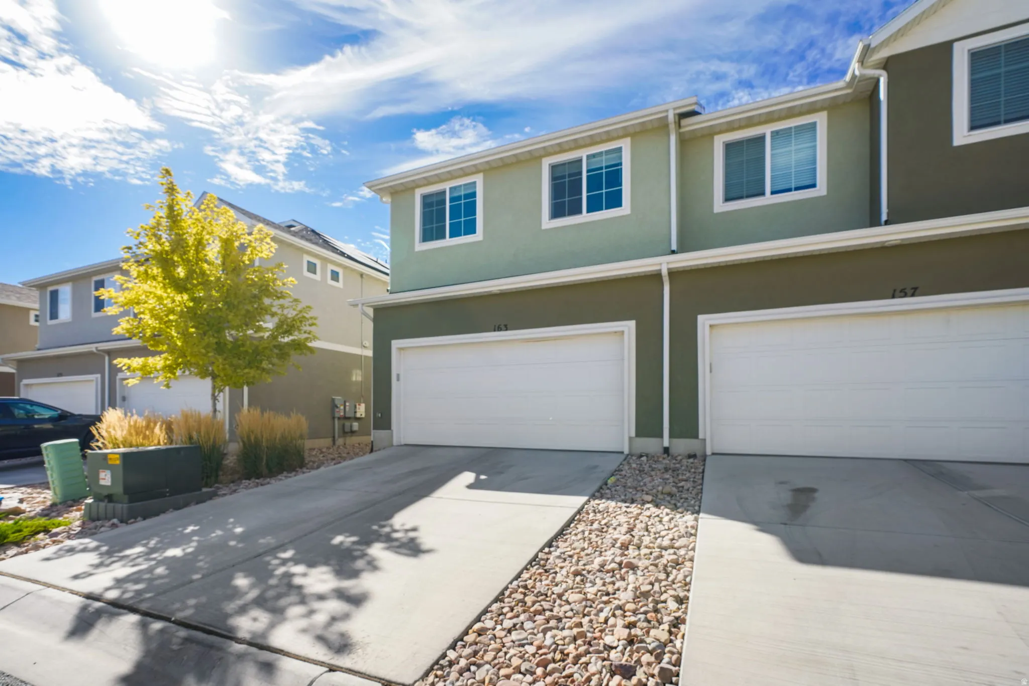Stucco exterior with white trim, concrete driveway, attached garage, and decorative rock landscaping