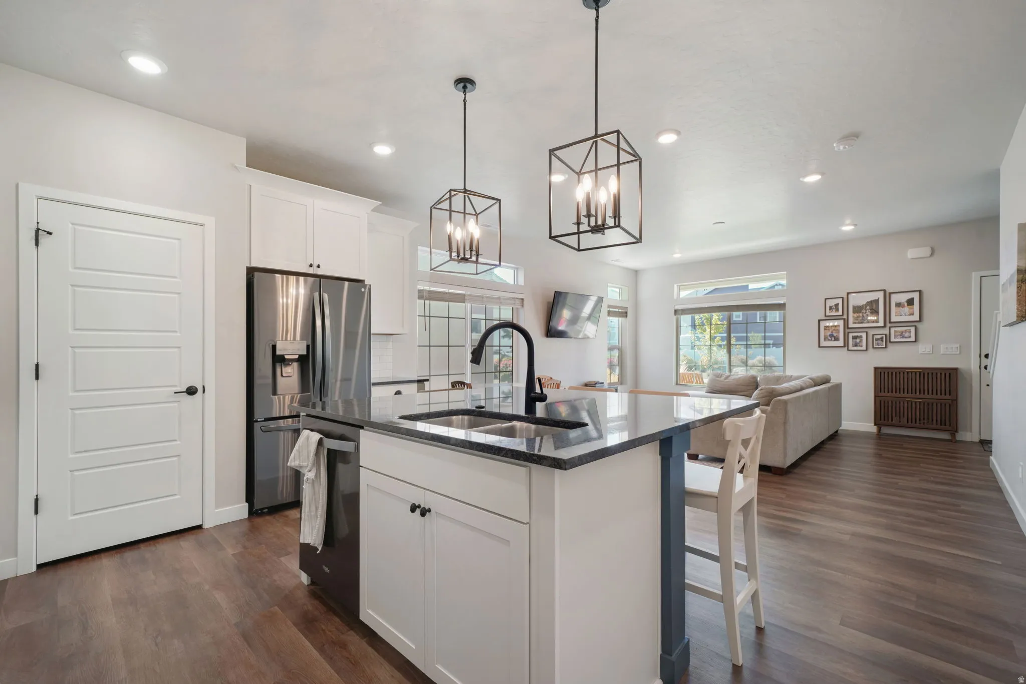 Kitchen island with integrated sink, stainless steel appliances, white cabinetry, wood-finish flooring, and recessed lighting